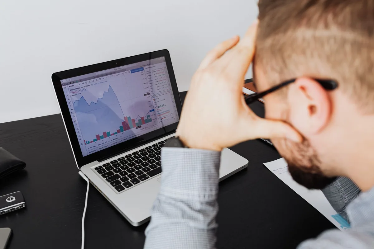 Unternehmer stützt den Kopf in die Hand, auf dem Laptop eine fallende Kurve